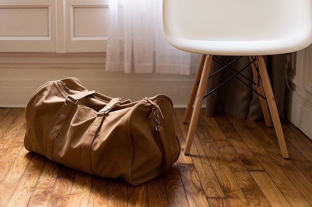 A packed duffle bag says ready to go and an inviting chair says ready to stay