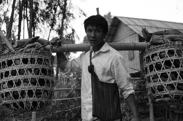 Honest young working man balancing two baskets of goods on a bamboo pole on his shoulder